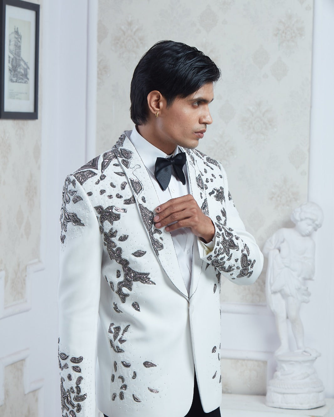 A man wearing a white tuxedo jacket with black floral embroidery, a white shirt, and a black bow tie | Aditya Bhardwaj