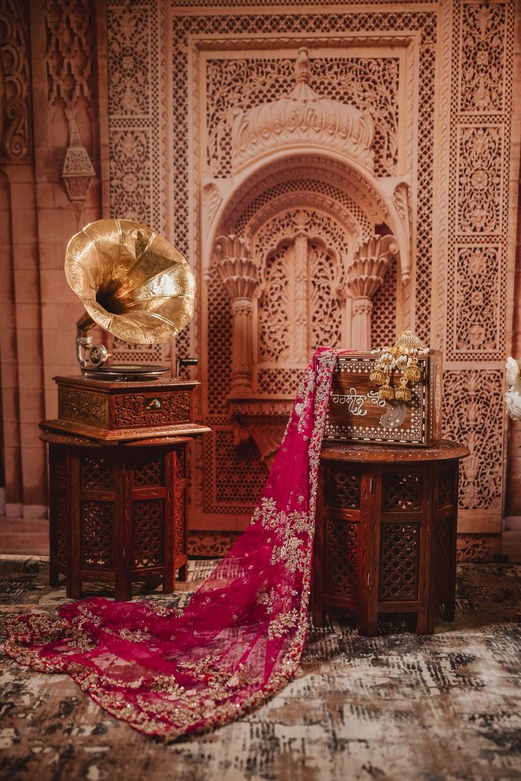 Decorative setup with a gramophone, red fabric, and intricate wall designs in a room.